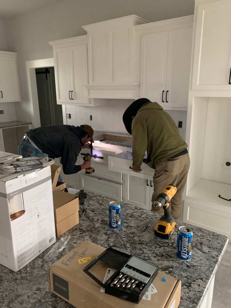 Dos instaladores ajustan un cajón de gabinetes blancos en una cocina.