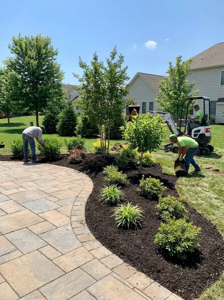 Equipo de jardinería acondiciona un jardín residencial con árboles, plantas y césped junto a un patio.