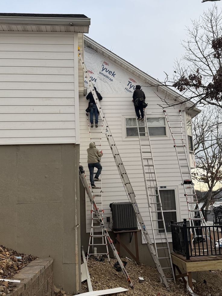 Tres trabajadores instalan revestimiento exterior blanco en la fachada de una vivienda.